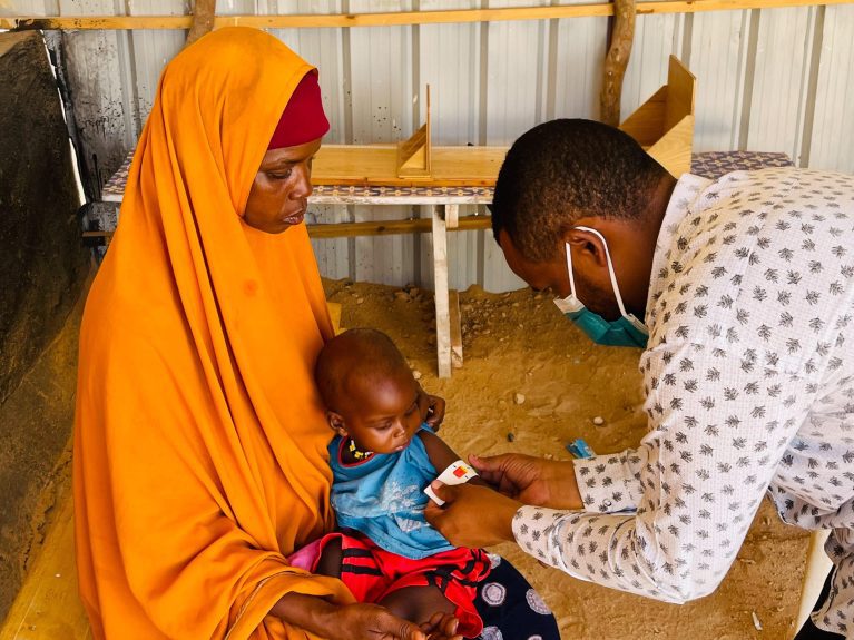 Somalia, Gesundheitszentrum in Bentiu, Mutter mit Kleinkind, Mann untersucht Kleinkind