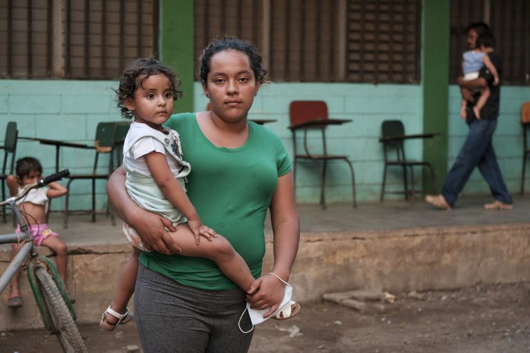 Frau mit Kind vor Gemeinschaftsunterkunft in Honduras