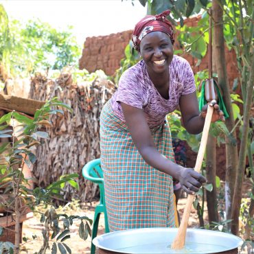 Frau kocht im Freien in einem großen Topf – im Rahmen des GEAR-Projekts von CARE in Uganda und Ruanda zur wirtschaftlichen Stärkung von Frauen.