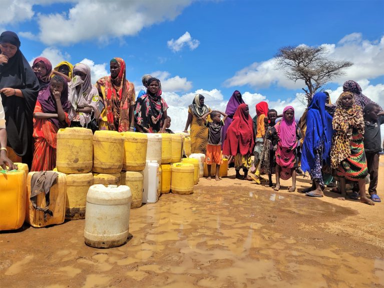 Frauen warten am Wasserhahn im Dadaab Refugee Camp, der von CARE installiert wurde, um ihre Kanister mit sauberem Trinkwasser zu füllen.