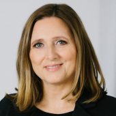 Porträt von Mag. Monika Lackner mit schulterlangen braunen Haaren vor hellem Hintergrund.