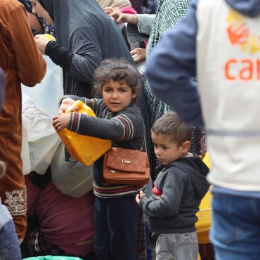 CARE im Nothilfeeinsatz in Gaza: Mitarbeitende koordinieren eine Wasserverteilung; Kinder und Familien warten mit Kanistern auf sauberes Trinkwasser und Unterstützung.