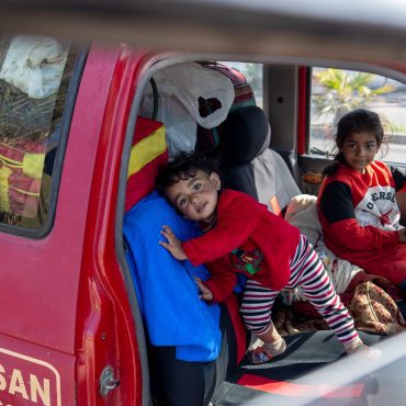 Kinder sitzen in einem alten roten Pickup, der mit Decken und wenigen Habseligkeiten beladen ist. Im Libanon befinden sich Tausende Familien auf der Flucht. Ihnen steht CARE mit Nothilfe zur Seite.