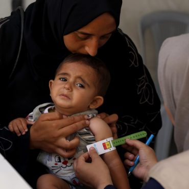 CARE-Helferin misst mit einem farbigen Band den Oberarmumfang eines Kleinkinds, um Anzeichen von Mangelernährung in einer Notunterkunft im Gazastreifen zu erkennen.