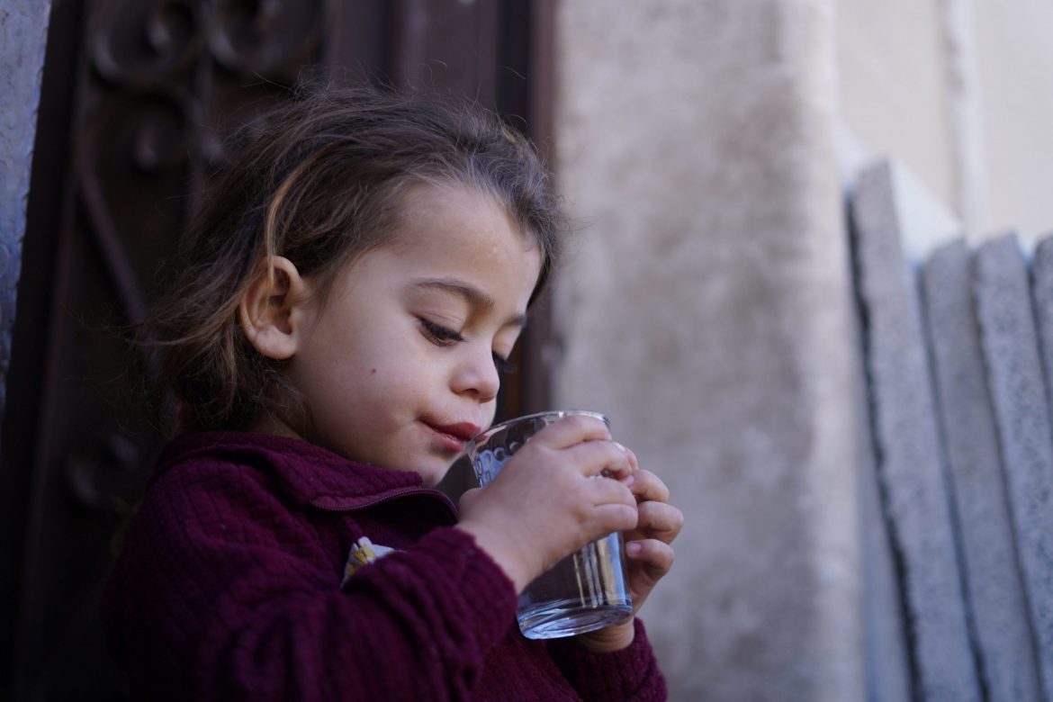 Kleines Mädchen trinkt aus einem Glas sauberes Wasser – CARE Österreich verbessert den Zugang zu sicherem Trinkwasser für Kinder in Krisengebieten.
