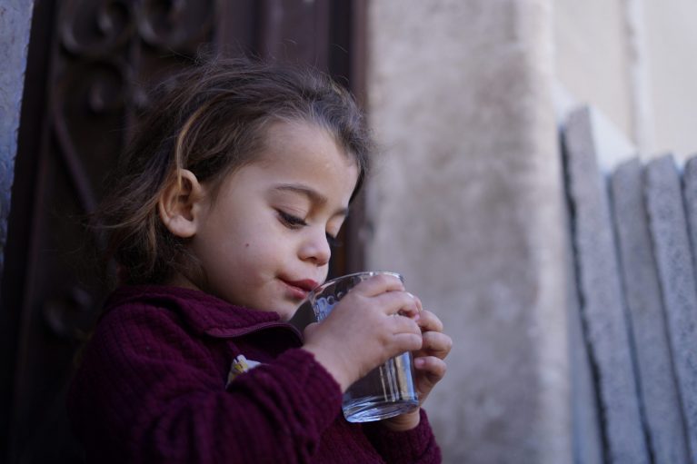 Kleines Mädchen trinkt aus einem Glas sauberes Wasser – CARE Österreich verbessert den Zugang zu sicherem Trinkwasser für Kinder in Krisengebieten.
